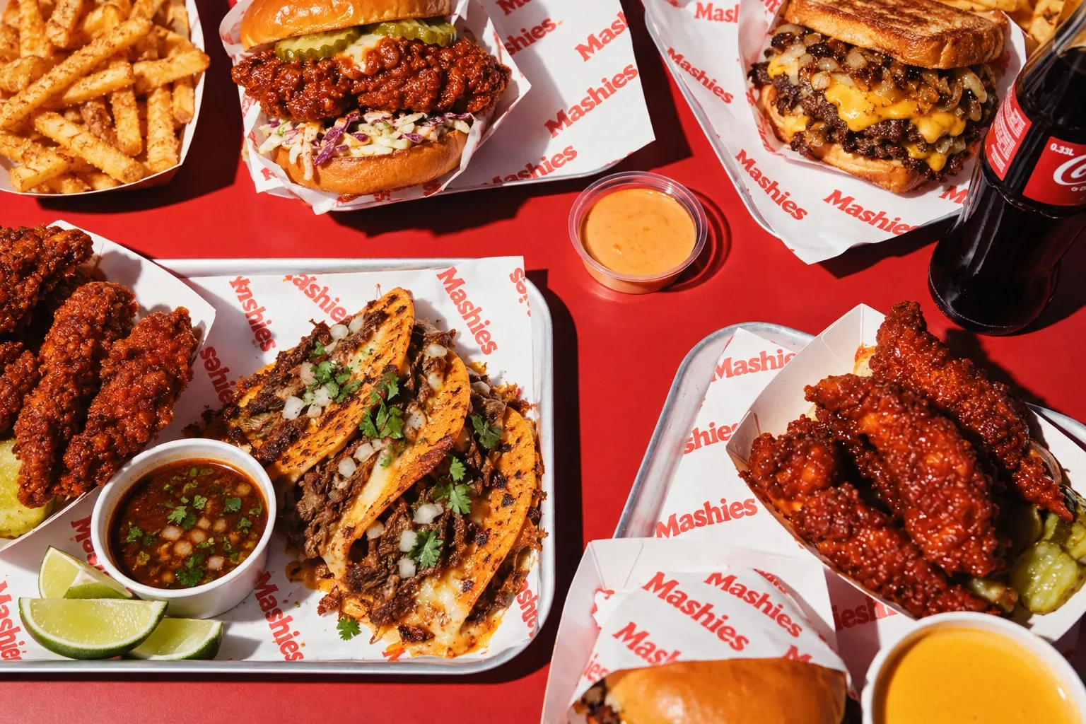 Birria Tacos, Nashville Tenders, Burger und Fries auf rotem Tisch